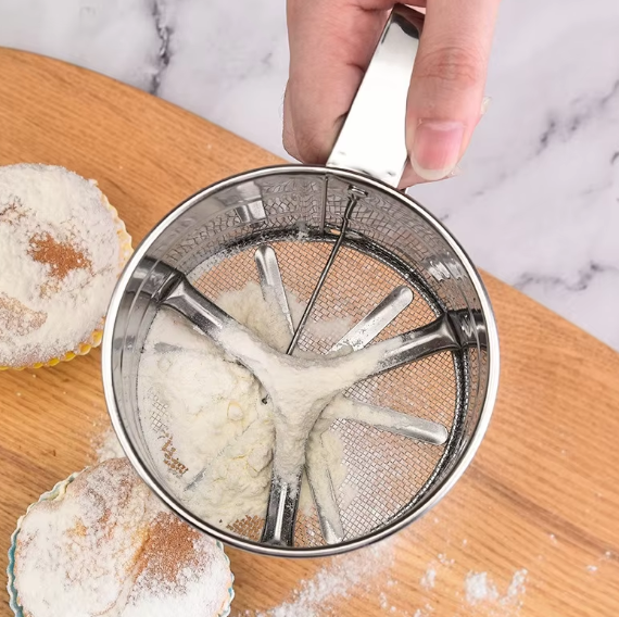 Stainless steel flour sieve cup with spring handle, fine mesh design for sifting flour, sugar, or cocoa powder, perfect for baking and decorating.